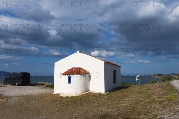 White building with a red roof by the sea, surrounded by a cloudy sky and peaceful countryside. A