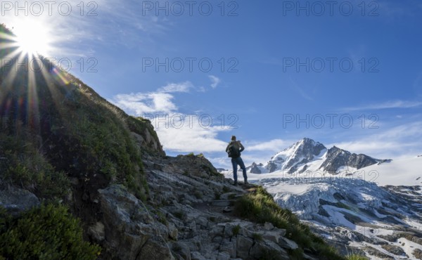 Mountaineer in front of high alpine mountain landscape with sun star, summit of Aiguille de