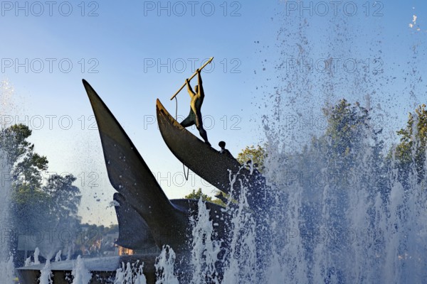 A dynamic statue surrounded by spraying water fountains at sunrise, memorial to the whalers of