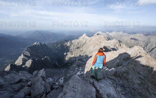 Mountaineer on a narrow rocky steep mountain ridge, view into the Höllental and to the Alpspitze
