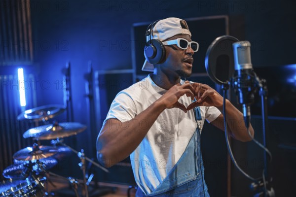 Young stylish male singer making heart shape with hands while recording new hit song in