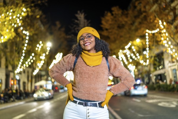 Young black woman tourist wearing yellow winter clothes and backpack, smiling with hands on her