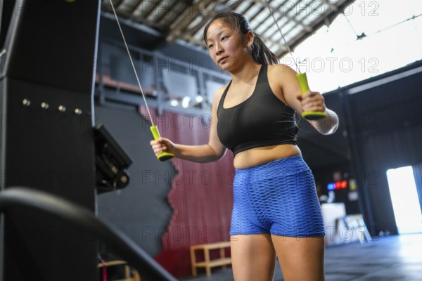Low angle view three quarter length photo of an asian woman training using lat machine to pull