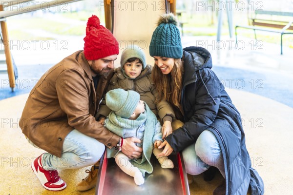 Parents assisting their children as they joyfully slide down a playground slide, embracing the fun