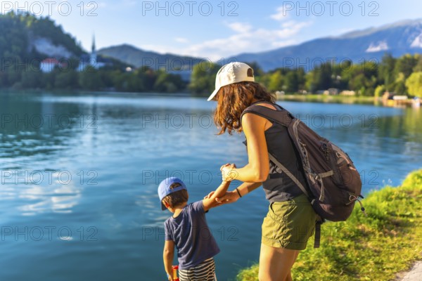 Mother and son holding hands, enjoying summer vacation by the turquoise water of lake bled, with