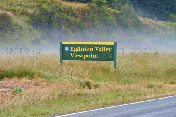 Sign showing the way to Eglinton Valley viewpoint, surrounded by misty pasture, summer, Milford