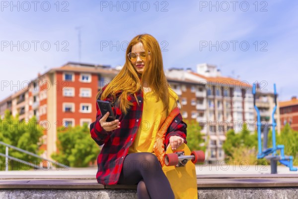 Skater woman in a yellow t-shirt, red plaid shirt and sunglasses, sitting with skateboard in the