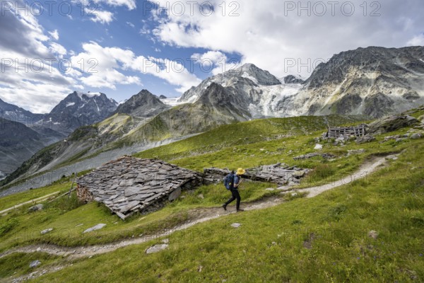 Mountaineers on a hiking trail, Alpine huts covered with slate slabs, mountain landscape near