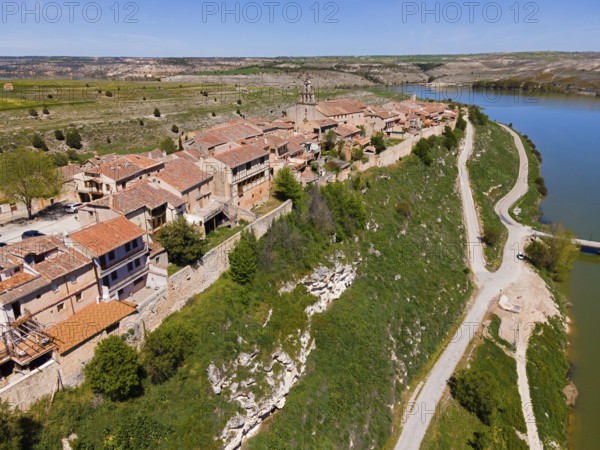 A village on a river with a raised road and green surroundings as well as densely built-up houses,