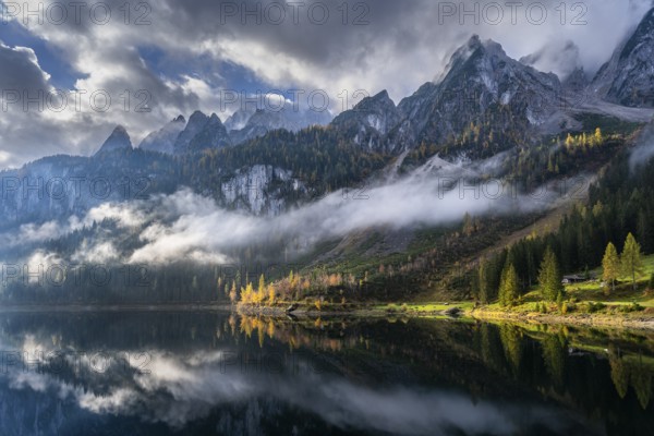 The Vordere Gosausee in autumn with a view of the Gosaukamm. Cloudy sky with sun. Trees in autumn