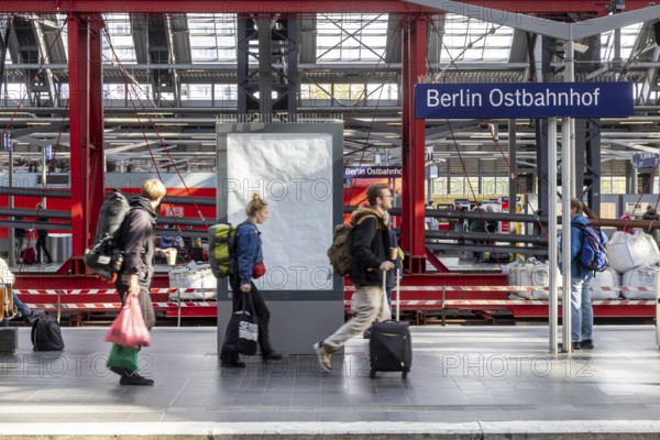 Construction site at Ostbahnhof station with station sign, travellers on the platform. Berlin,