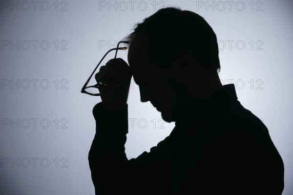 Symbolic photo on the subject of overload. Silhouette of a man rubbing his aching head. Berlin,