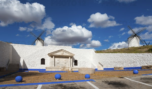 Two windmills and a stone wall against a blue sky full of clouds, Fuente del Caño, open-air museum,