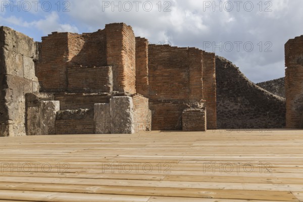 Wood plank decking and remnants of an old terracotta brick and stone wall structure at the ancient