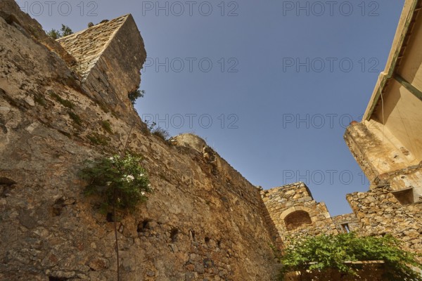 An old stone wall with vegetation and ruins under a bright blue sky, Venetian Sea Fortress, Leper
