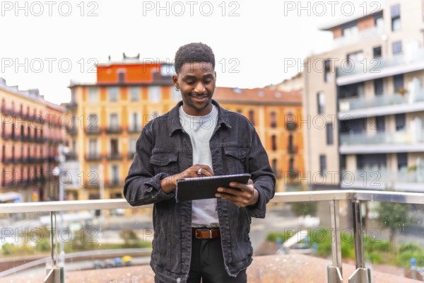 Frontal three quarter length photo of a happy young african man using digital tablet standing in a