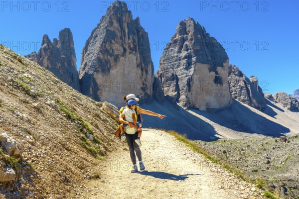 Woman carrying child hiking and pointing at the landscape near tre cime di lavaredo, dolomites, a