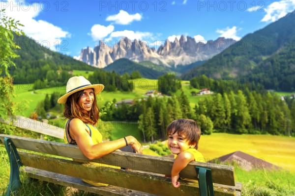 Mother and son relaxing on a bench enjoying the landscape of the odle mountains in val di funes in