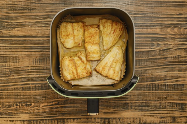 Five golden brown grilled fish fillets are neatly placed inside an air fryer basket. The background