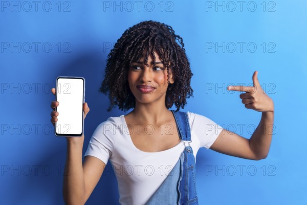 Studio portrait of a young woman holding a smartphone with blank white screen and pointing at it
