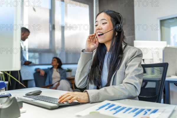 Young asian manager talking on headset and working on computer in a bright coworking office with
