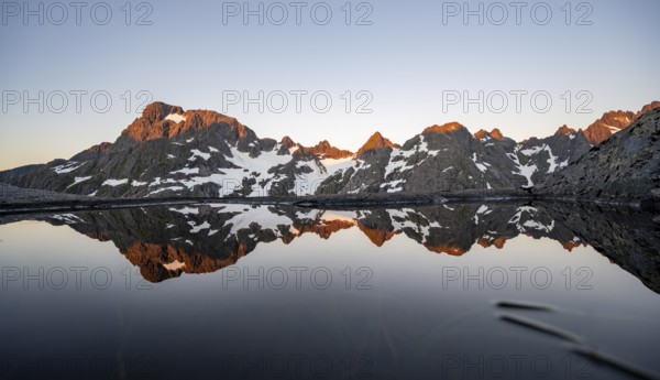 Rocky mountain peaks reflected in a small pond, mountain landscape with alpenglow at sunrise, at