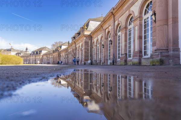 Large building with elaborate architecture reflected in a puddle under a blue sky, Schwetzingen