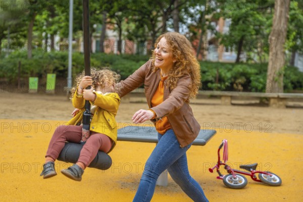Happy scene of a caucasian adult mother playing with a girl swinging in a park