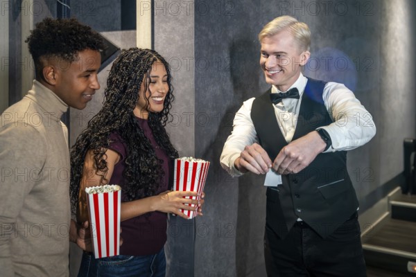 Young couple holding popcorn buckets entering a movie theater and checking their tickets with the
