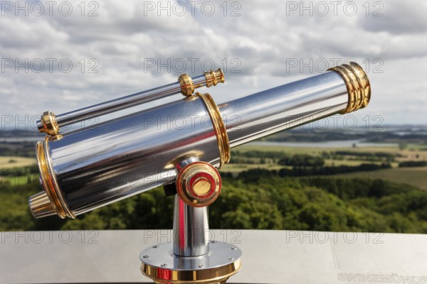 Metallic telescope points into the distance over a vast landscape under a cloudy sky, Rügen,