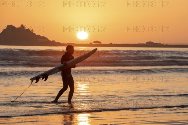Crescent City, California - A surfer takes his board out of the water as the sun sets over the
