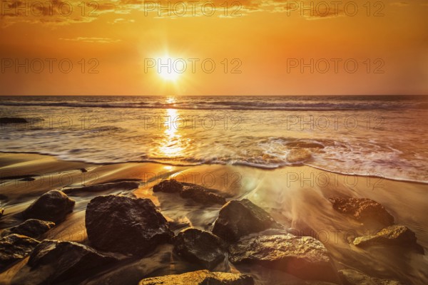 Tropical beach vacation background, waves and rocks on beach on sunset with beautiful cloudscape.
