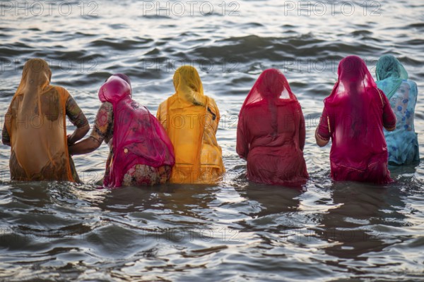Hindu pilgrims, woman in colourful saris, take a holy dip in the sea in front of sunrise at Ghat