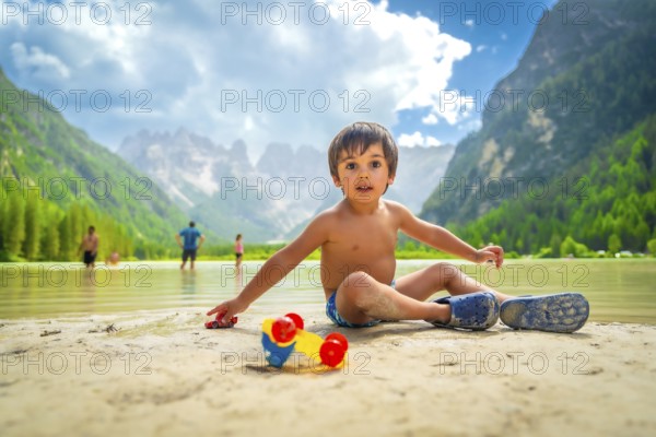 Young boy playing with toy cars on the sandy shore of lago di landro, surrounded by the stunning