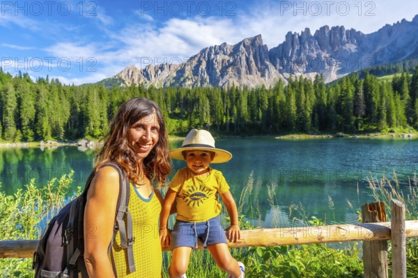 Mother and son enjoying the stunning scenery of lake carezza with the latemar mountain range in the