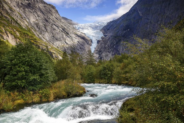 River flanked by mountains flows through a green valley with a view of the shimmering