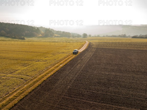 Landscape shot of a car on a path between golden and brown fields in sunlight, electric car VW ID5,