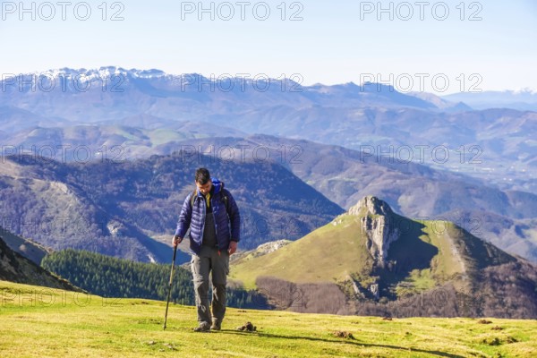 Male hiker walking on a grassy mountain slope with scenic views of the pyrenees mountains in the