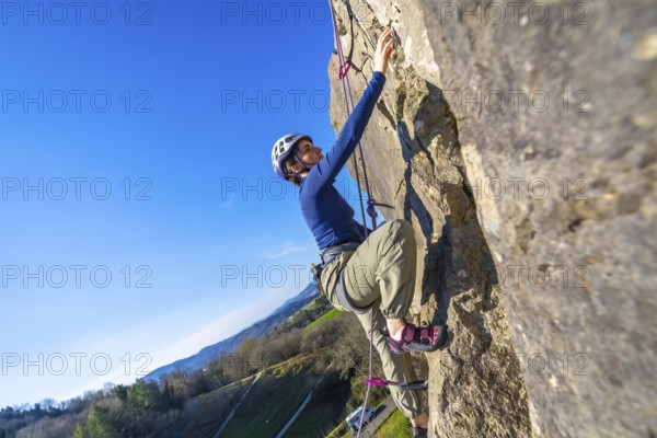 Female climber ascending challenging rock face on a sunny day, enjoying the thrill of outdoor