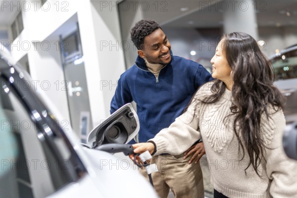 Smiling couple examining the charging socket of an electric vehicle while exploring options at a
