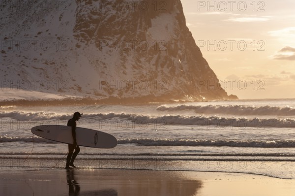 Surfer with surfboard under his arm on the beach of Unnstad, winter surfing, Lofoten Island