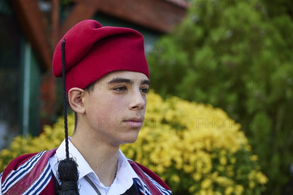 Side portrait of a boy in traditional Cretan traditional costume with a red hat outdoors, visit of