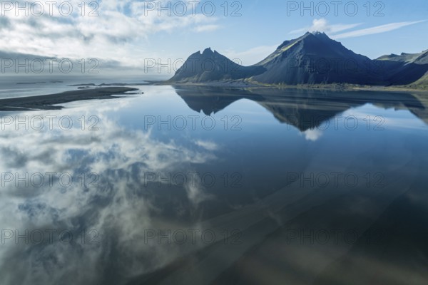 Aerial view over the calm sea to Mt. Brunnhorn and Vestrahorn, east of Höfn, clouds are reflected