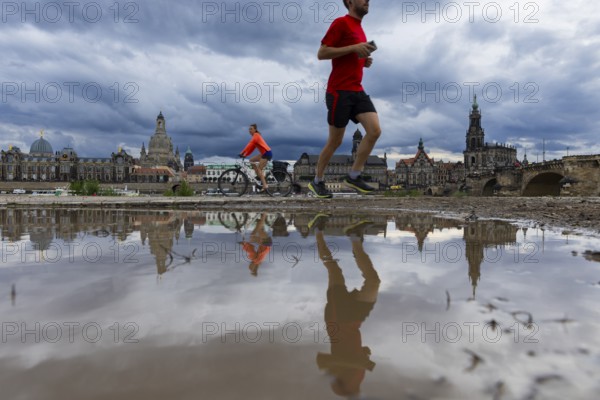 The silhouette of Dresden with a cyclist and a jogger and dark clouds behind the Church of Our