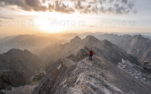 Mountaineer with helmet on a narrow rocky ridge at sunrise, crossing the Jubiläumsgrat, view of