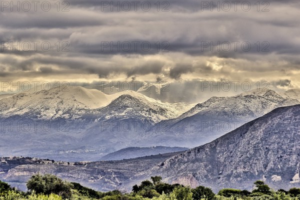Snowy mountains under threatening grey clouds in a vast landscape with a dramatic atmosphere, Lefka