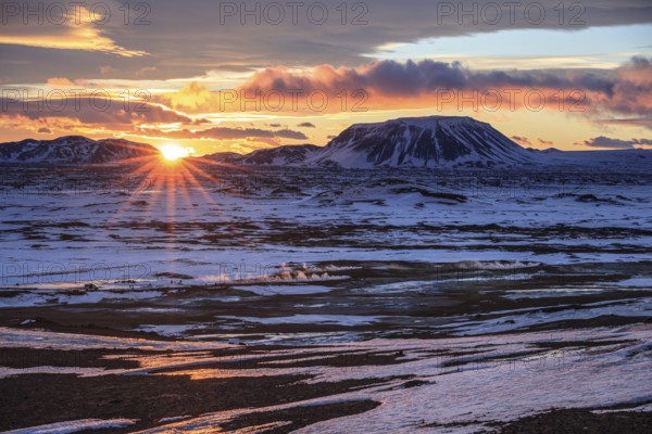 Hot springs and geothermal area in front of mountain landscape in winter, sunbeams, cloudy mood,