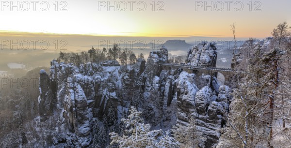 Snow-covered rock castle Neurathen and Bastei bridge in the morning, in the background the