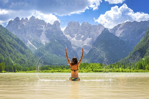 Young woman raising arms and splashing water in the famous lago di landro, also known as durrensee