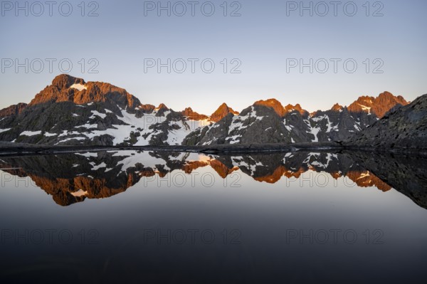 Rocky mountain peaks reflected in a small pond, mountain landscape with alpenglow at sunrise, at